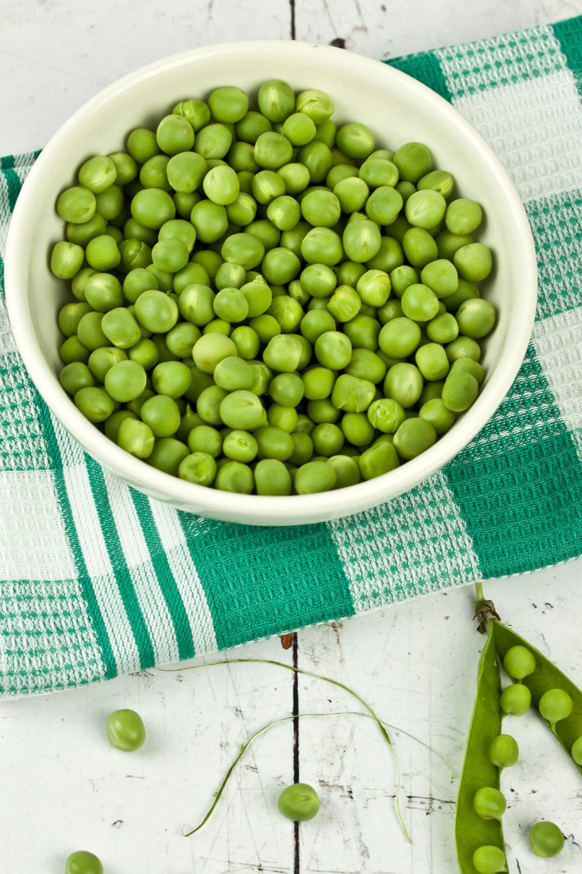bowl of green peas on table with checkered towel.